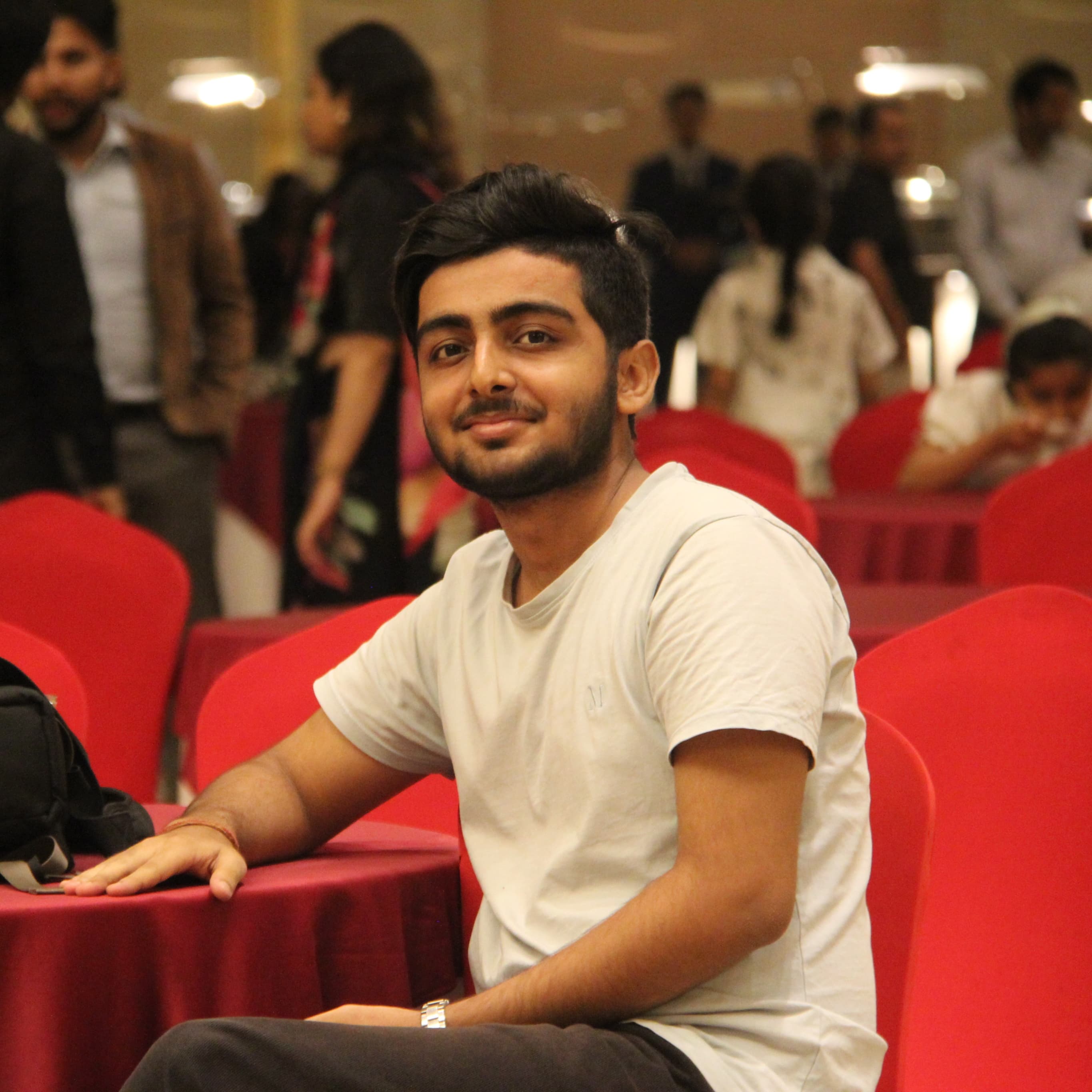 Sanchit Pandey seated in a hall of red chairs at a tech event