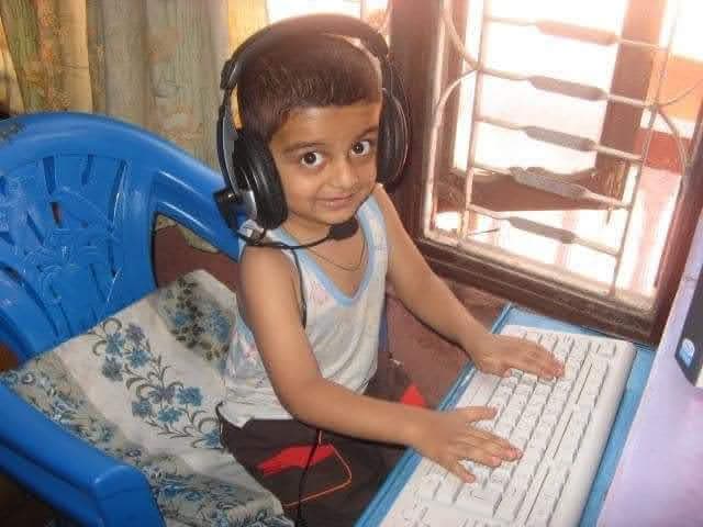 A childhood photo: a young boy wearing headphones at a desktop keyboard